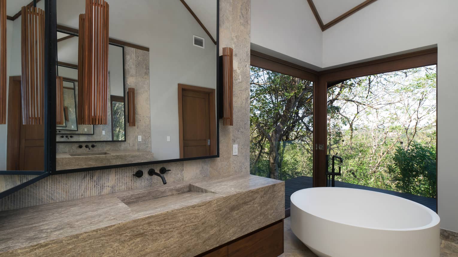 Modern bathroom with round standalone tub, windows with greenery