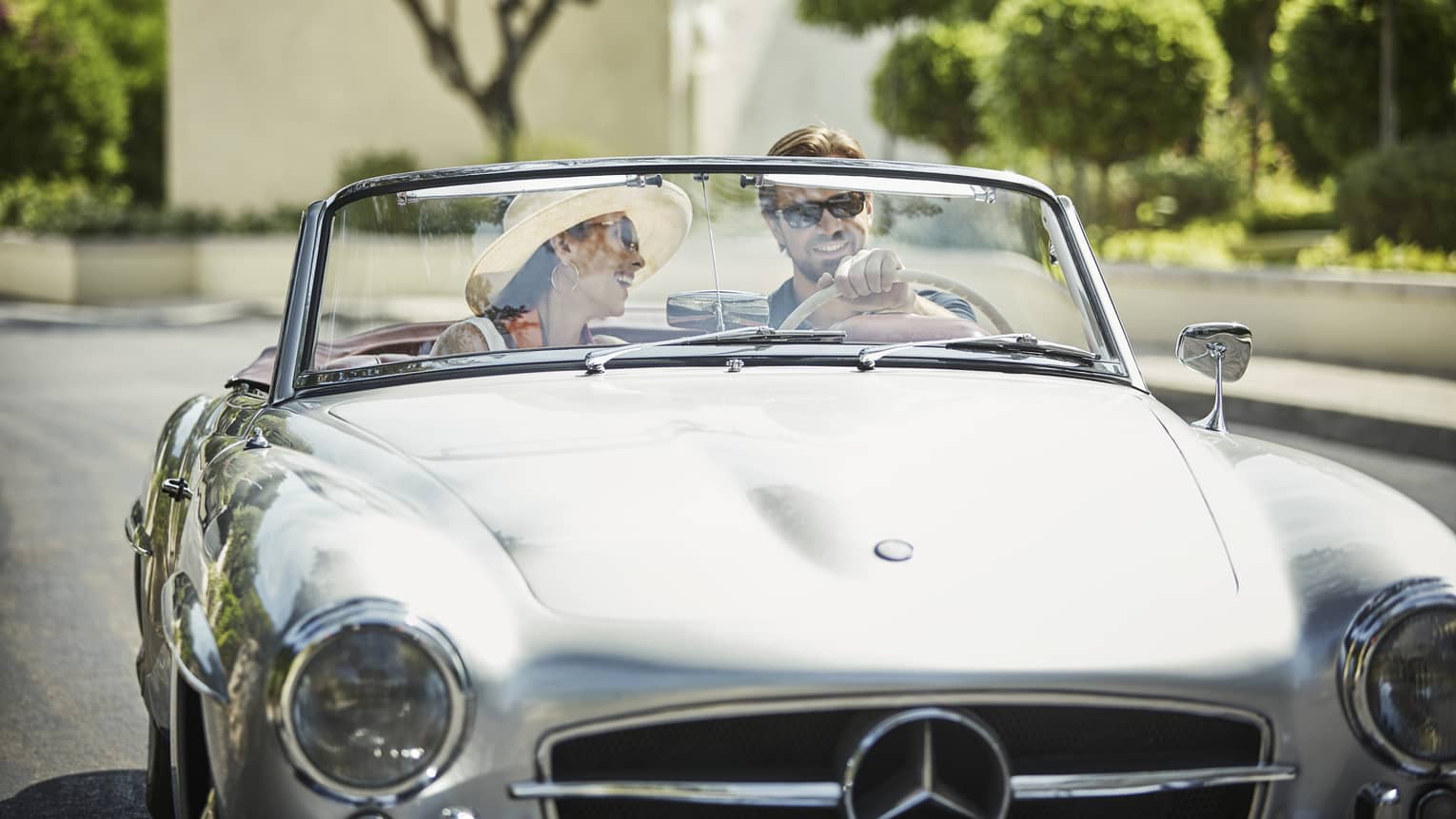 Smiling couple drive in silver luxury convertible car on sunny day