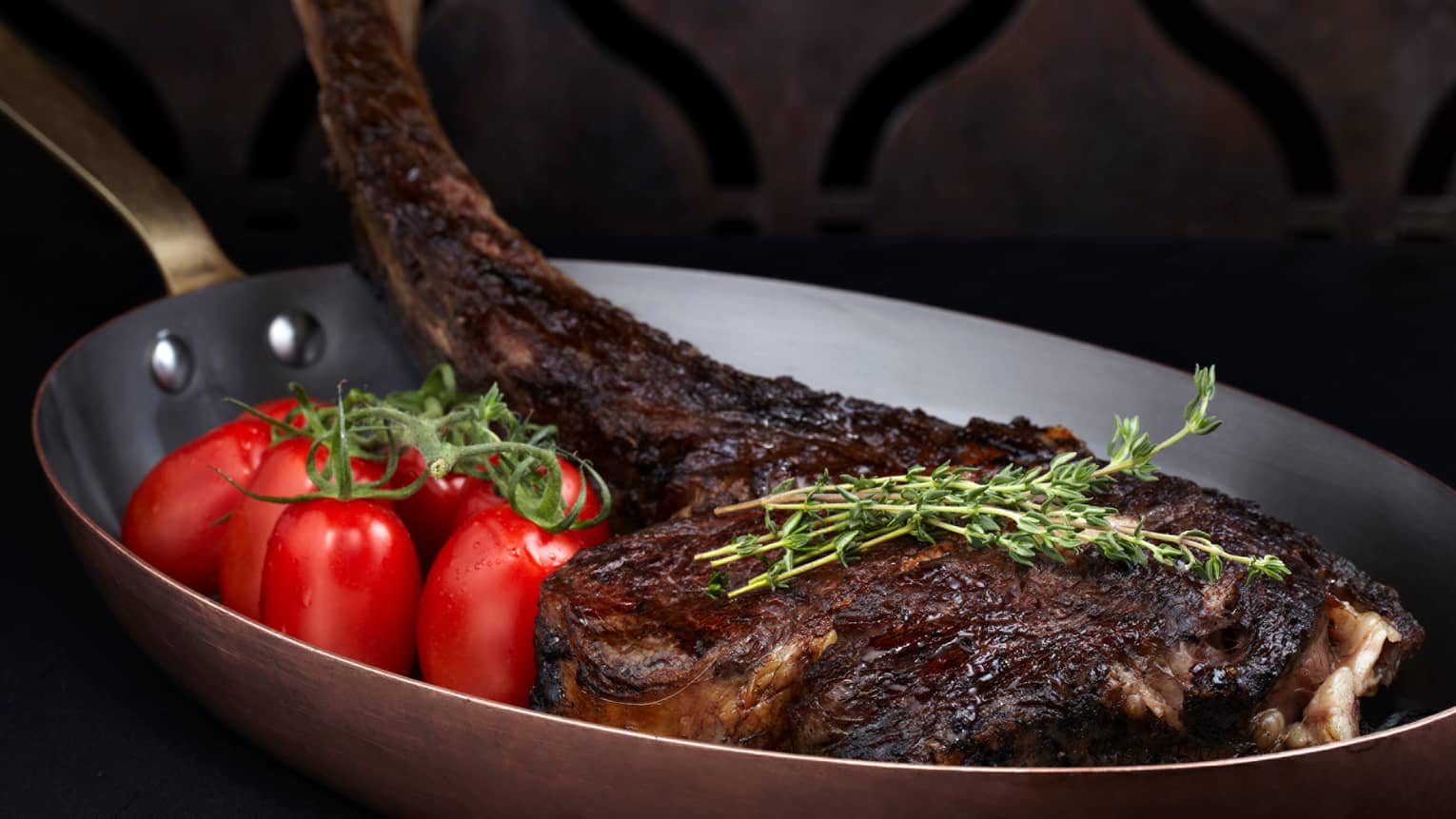 Wagyu beef tomahawk 30 ounce grilled chop in pan with whole tomatoes, herbs