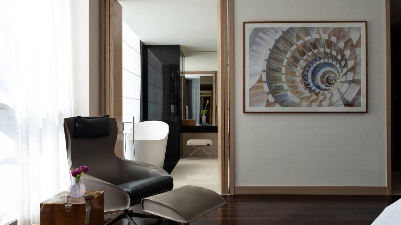 Black arm chair and ottoman in the corner of a room, artwork on wall