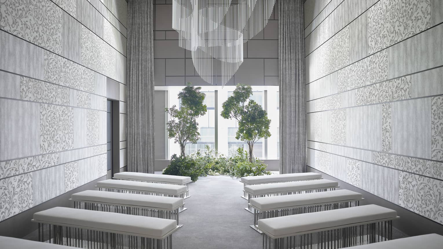 Modern event room, rows of plush benches face window and potted trees
