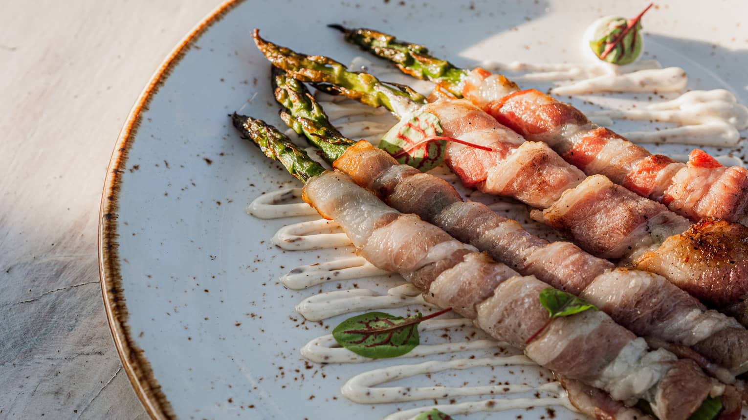 Asparagus wrapped in ham on white ceramic dish