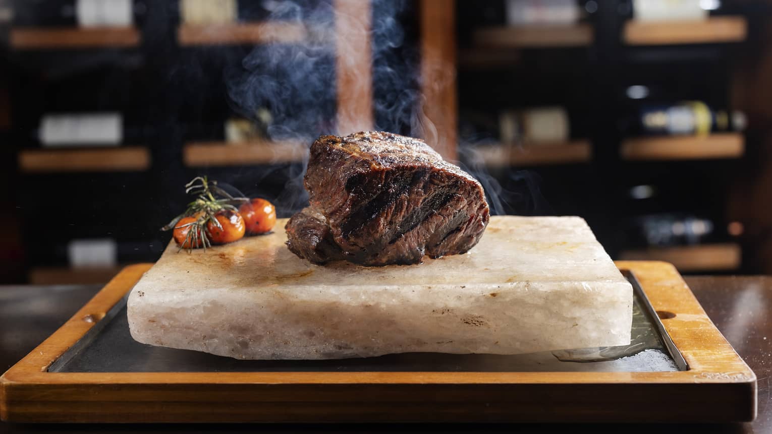 Steaming cut of rib-eye steak served on a slab of marble with roasted cherry tomatoes on the side