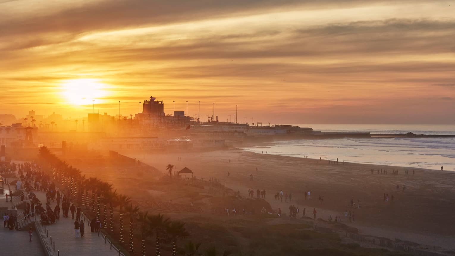 Orange sunset over Casablanca beach, silhouettes of people walking along boardwalk
