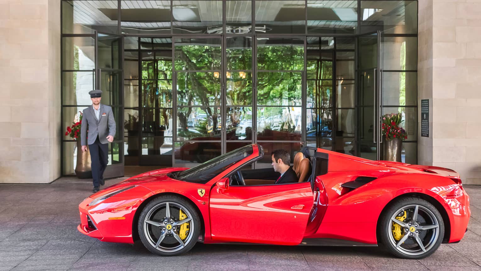 Hotel staff walks towards man in driver's seat of red sports car at Four Seasons Hotel Austin entrance
