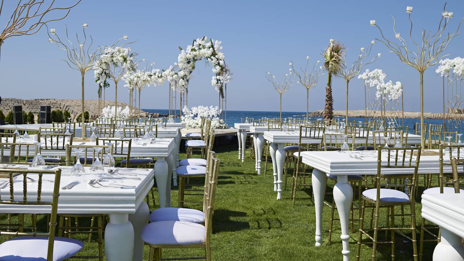 Oceanfront lawn set for a wedding with white tables, gold chairs and white orchids