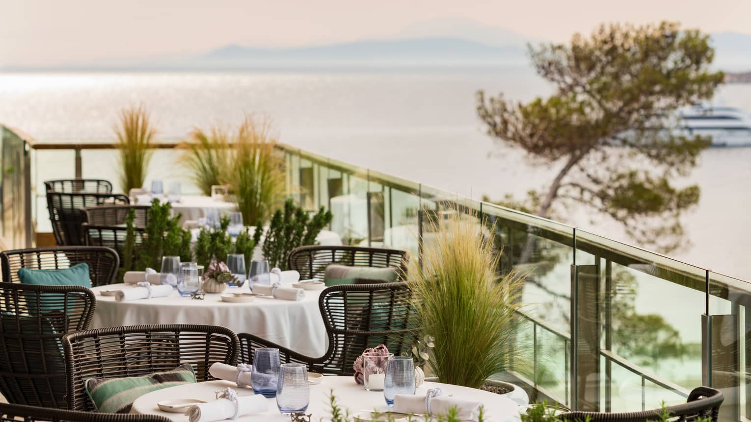 Round dining tables, each with three modern chairs, on restaurant terrace overlooking the sea in Athens