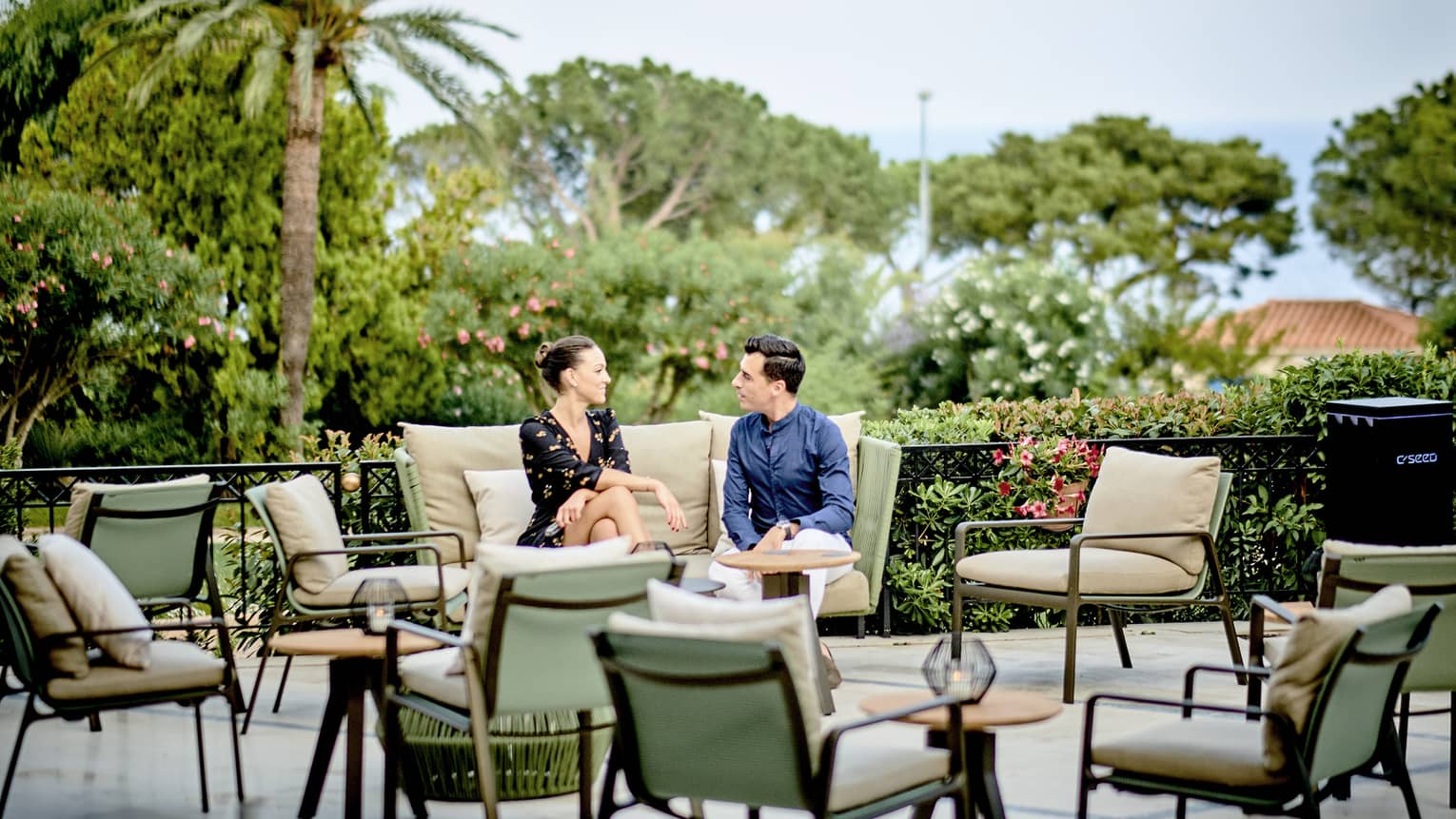 Le Bar terrace with couple seated on beige settee, light-green chairs and beige cushions