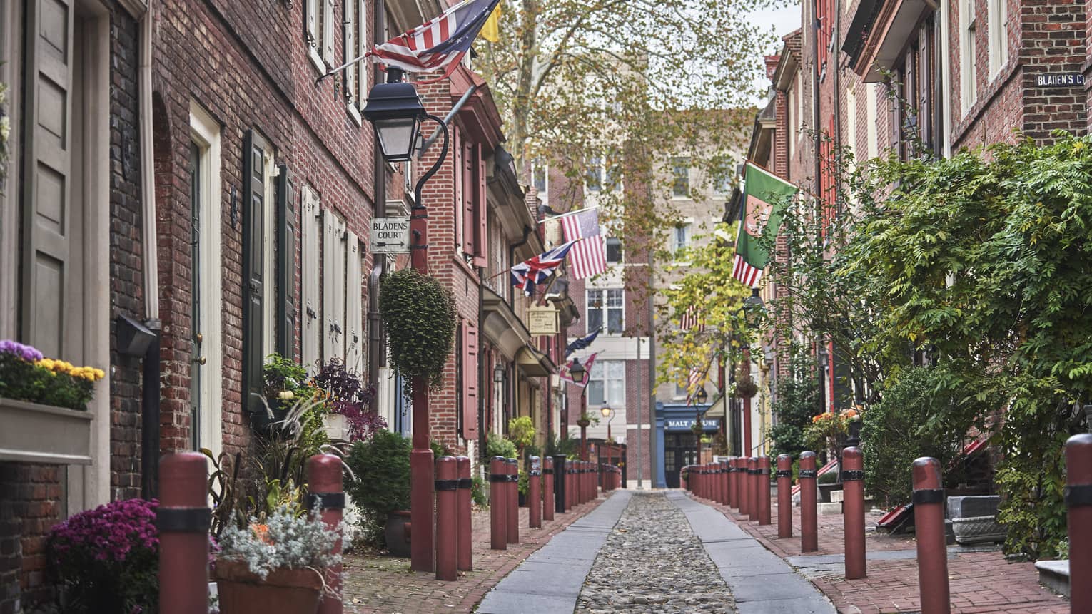An old cobble-stone street lined with charming brick buildings, plants and patriotic flags