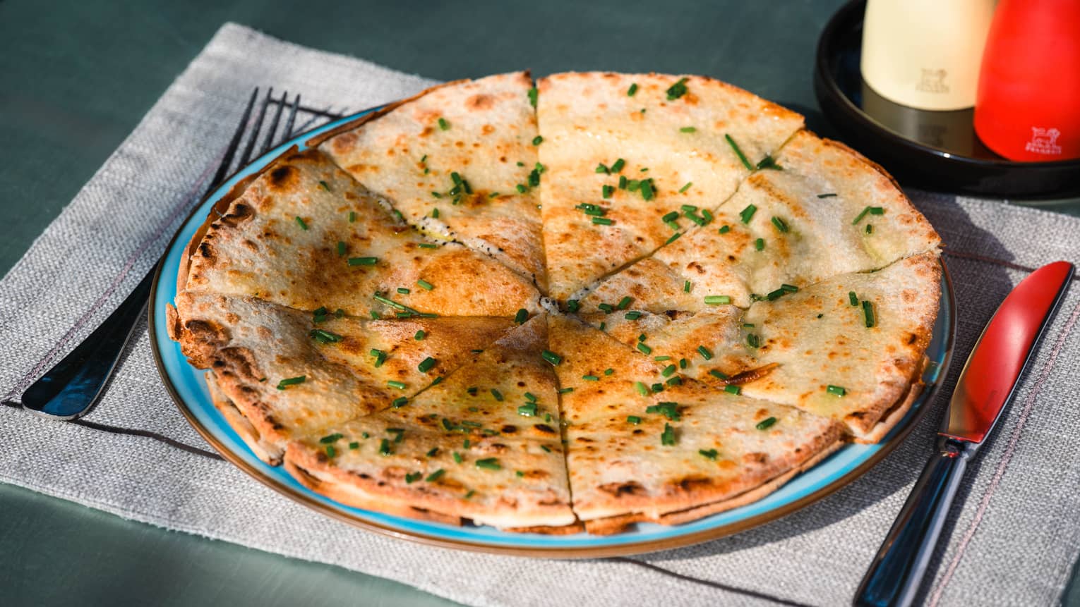 Focaccia round cut into triangles and dusted with chives on blue plate
