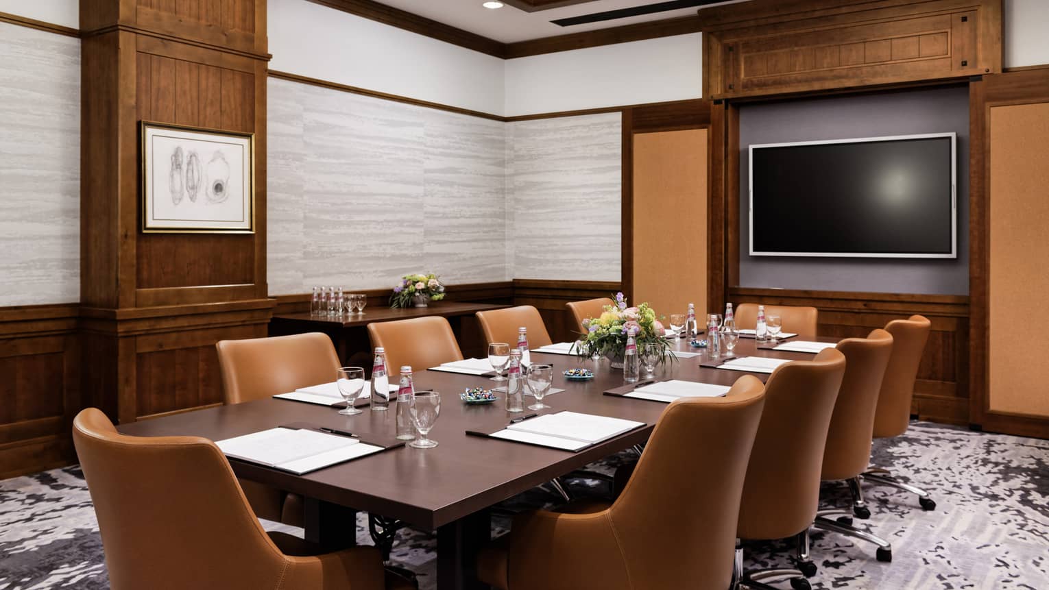 A meeting room with a long table, brown chairs and a screen on the wall.