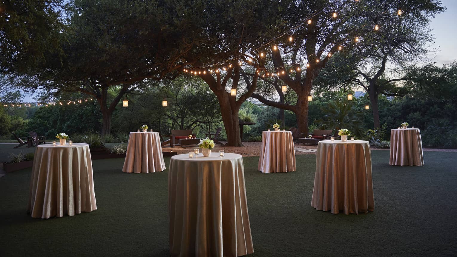 Small cocktail tables with silk linens across event lawn at night