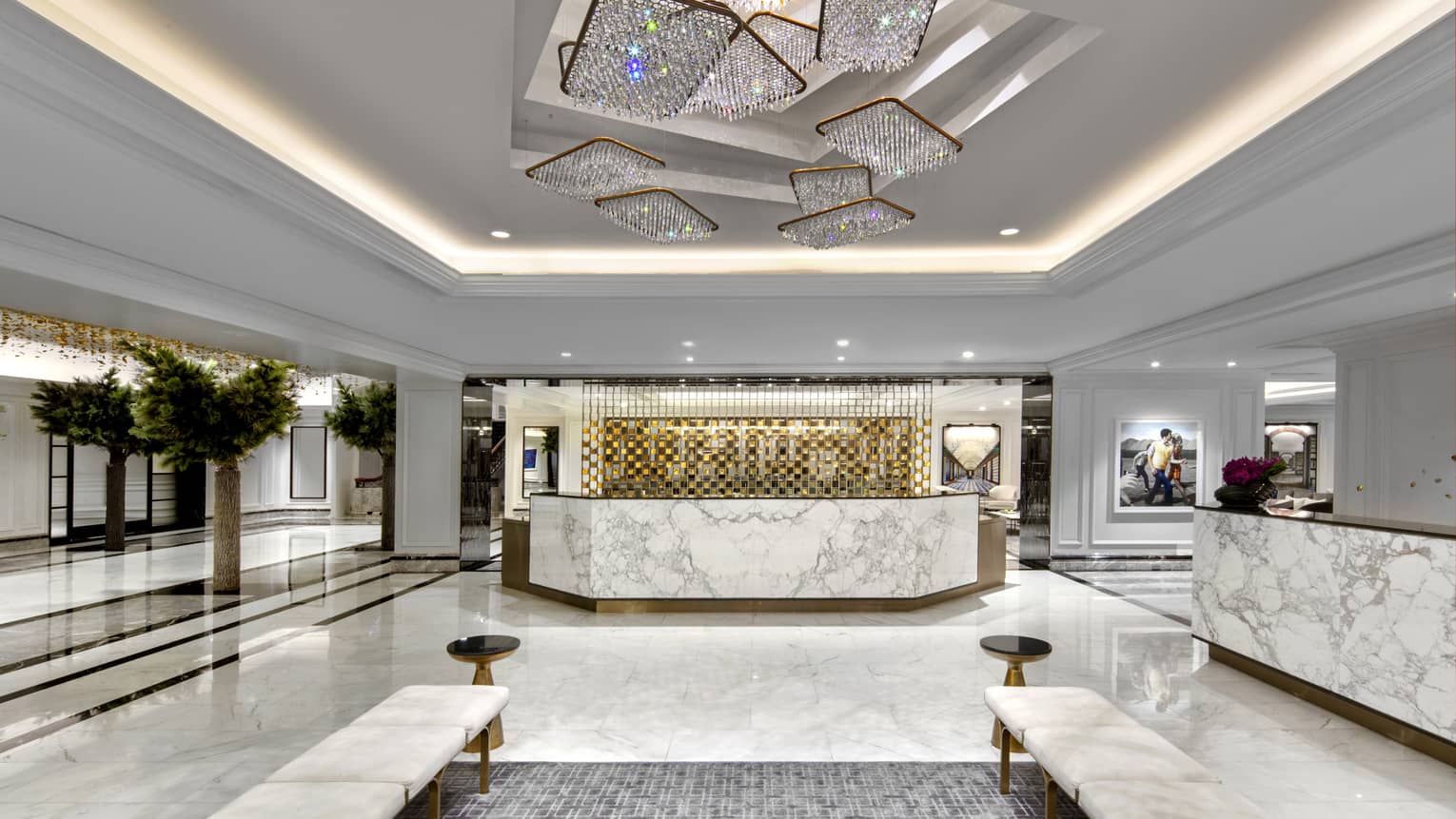A hotel lobby with white and grey marble features and a large reception desk.