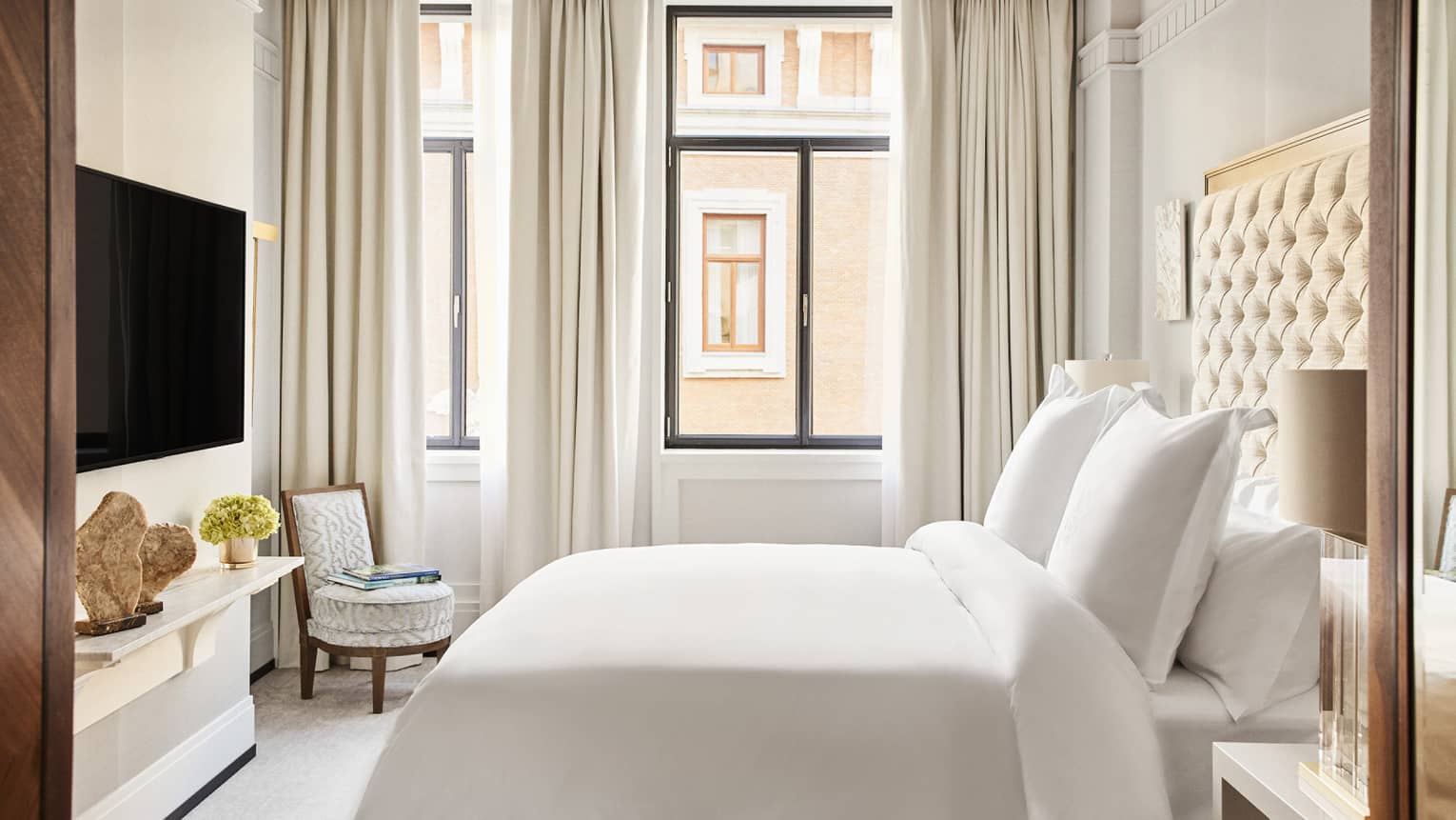 Hotel room with king bed, white linens, floor-to-ceiling curtains, TV