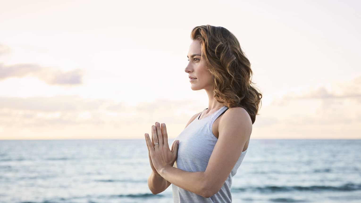 Woman with hands in prayer pose, acting calm on a beach with the ocean in the background