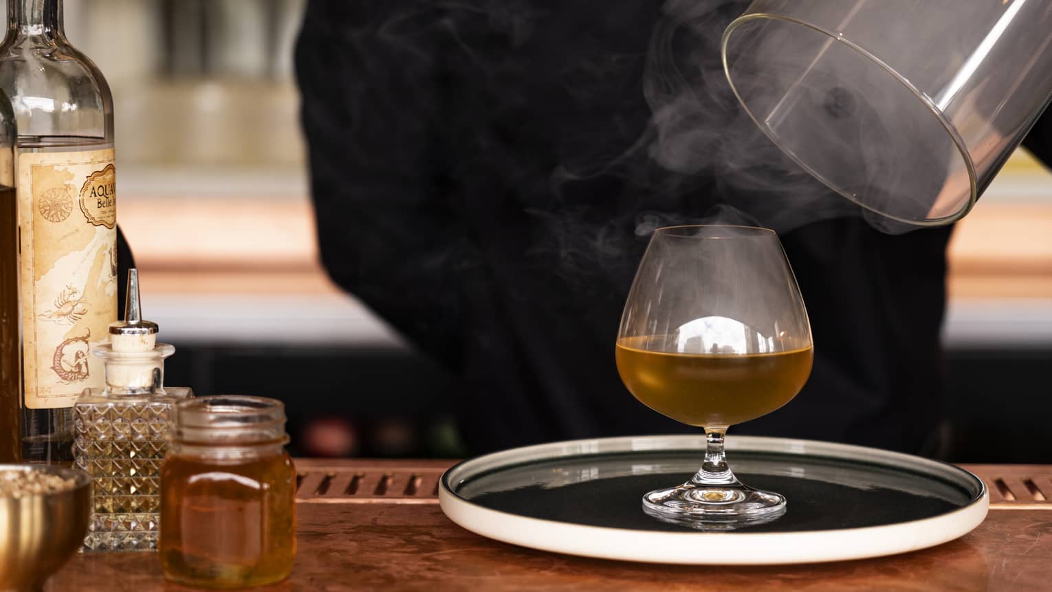 Bartender lifts cover from platter with steaming Old Gods Cocktail