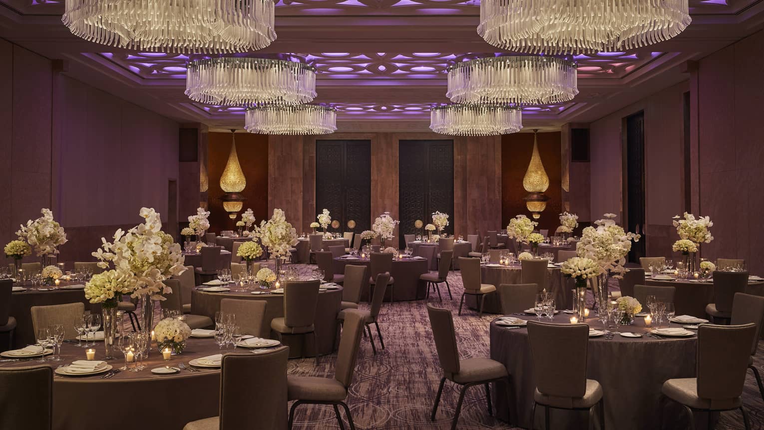 Round banquet dining tables in ballroom with round chandeliers, purple lights on ceiling