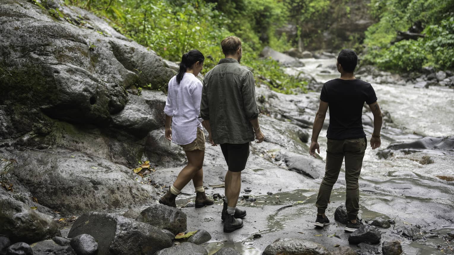 Three people walk along the rocks along the edge of a river