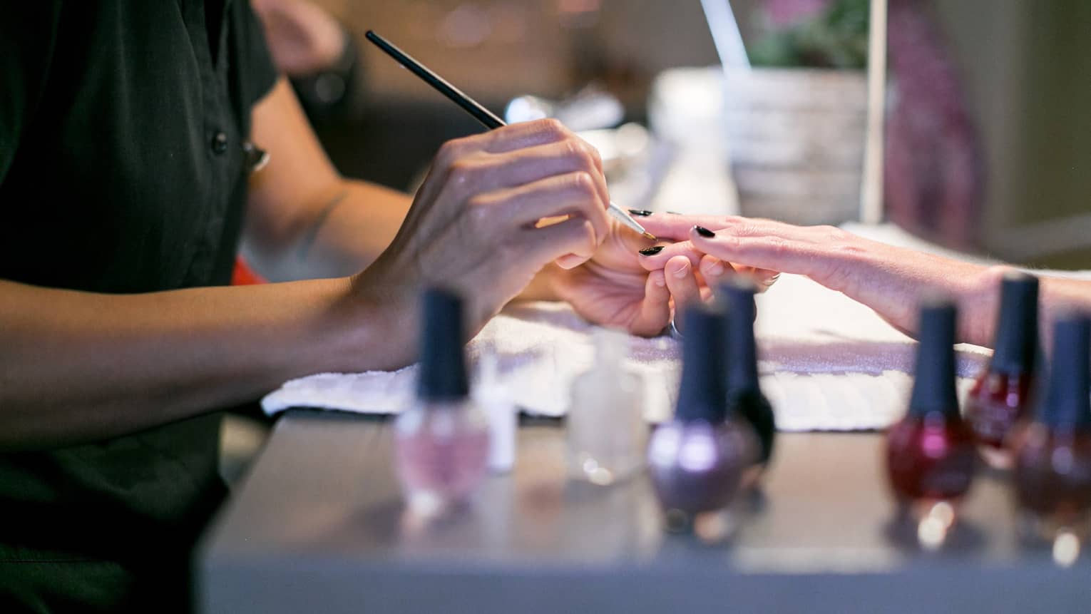 Close-up of spa staff painting woman's nails at manicure table