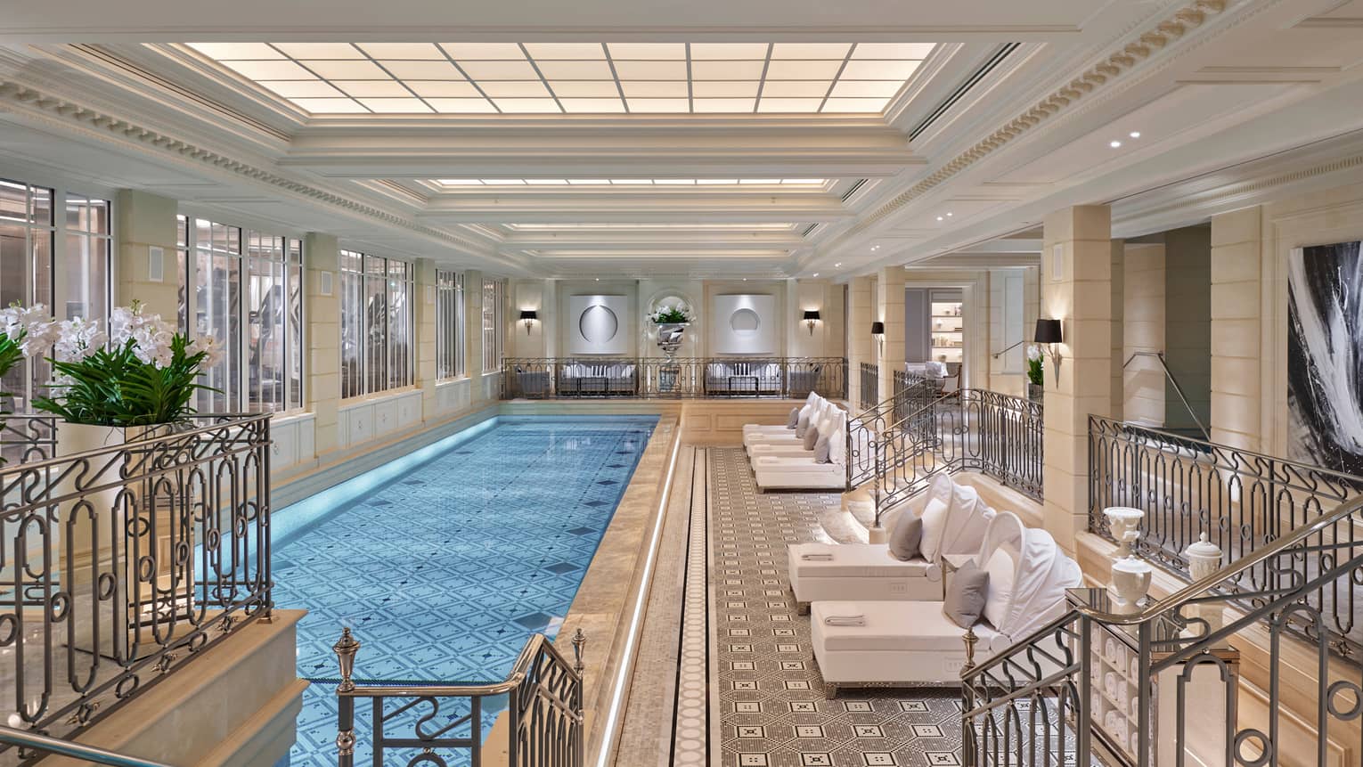 Long, elegant indoor swimming pool lined with plush white patio lounge chairs