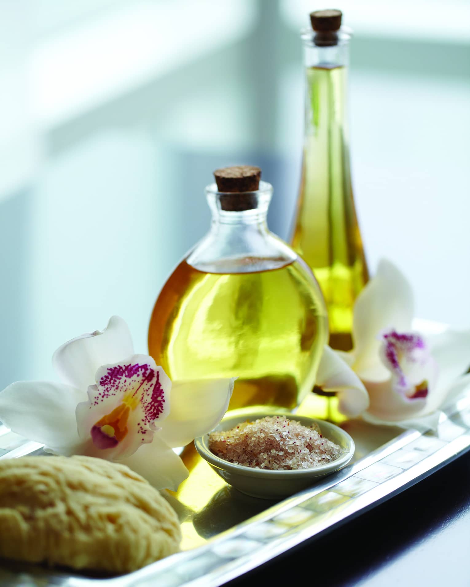 Close-up of small spa bowl with salt scrub, glass bottle with oil, white and purple tropical flower