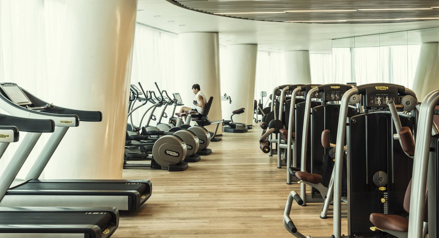 Cardio machines in bright fitness room with modern white pillars, man on bicycle machine