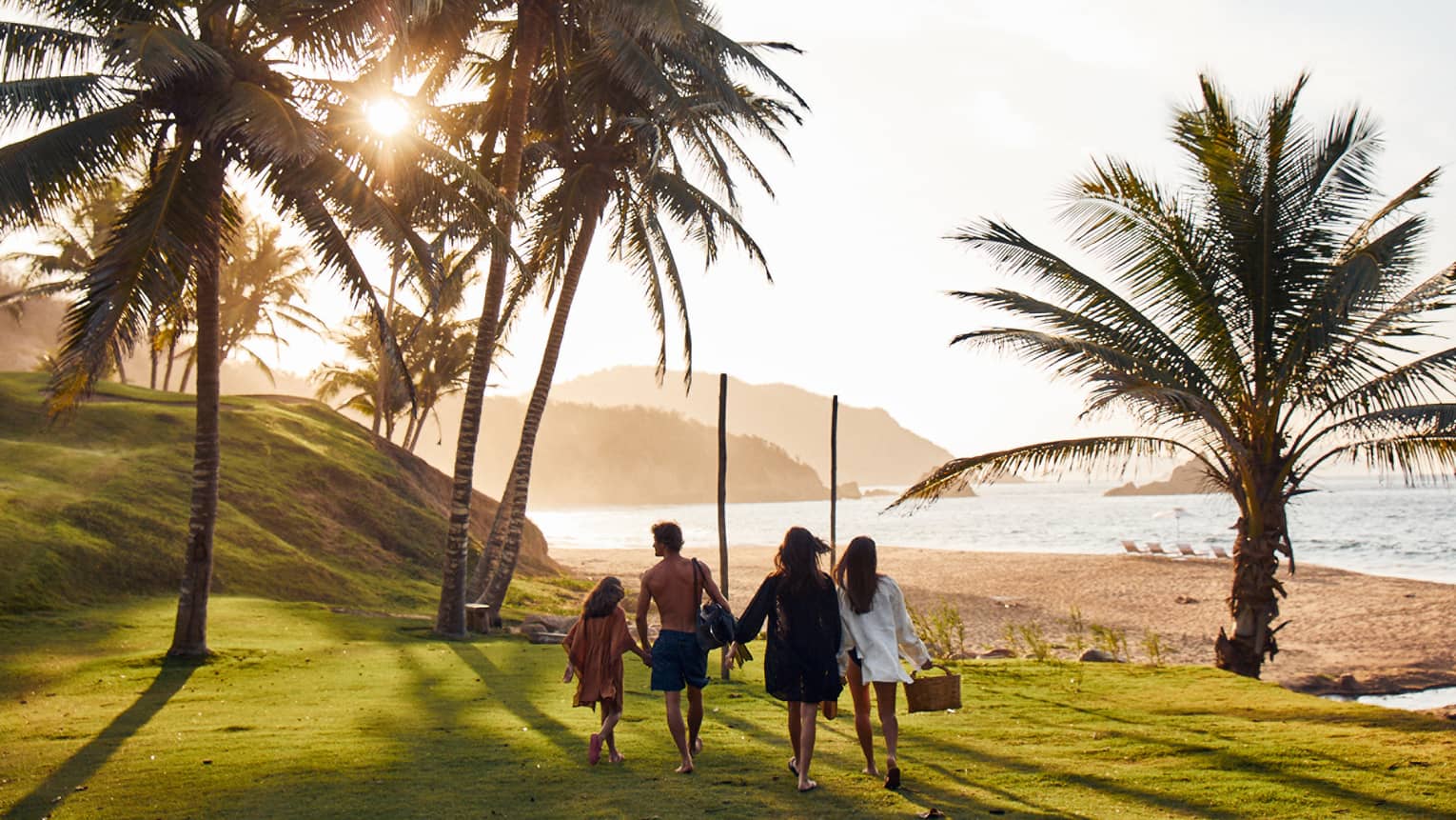 A family walking on well-cut grass with palm trees around.