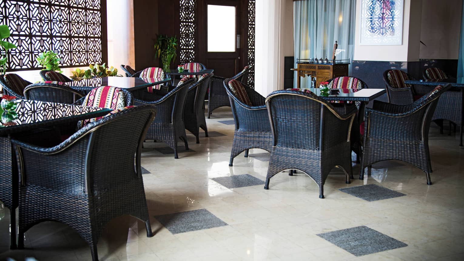 Dining room with two white pillars, three black square tables, each with four black chairs, black and white tile floor