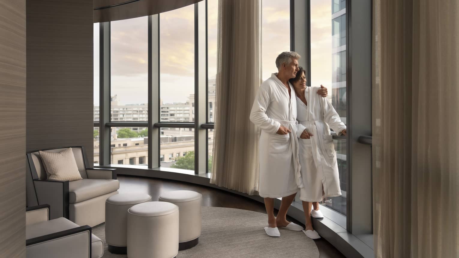 A man and woman in spa robes looking out a window.