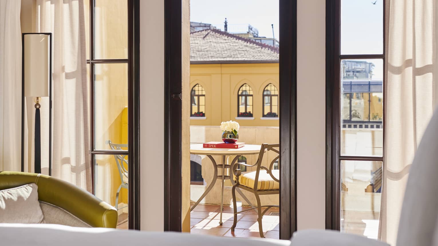 Hotel suite’s tall dark-framed windows with view onto terrace with café seating across from historic building