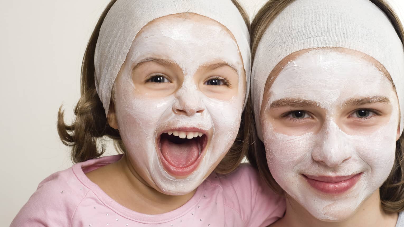 Two young girls with white clay spa masks on faces, towel wraps around foreheads