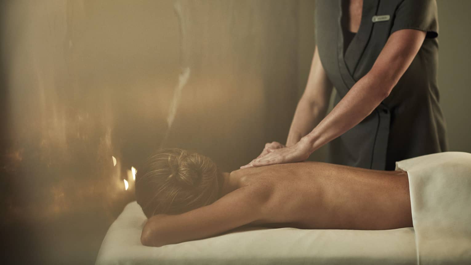 A woman laying on a massage bed being given a massage by a staff member.