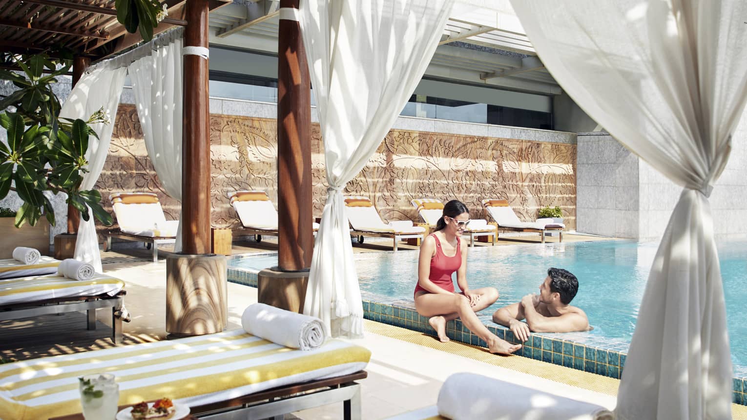 A couple lounges in the pool near a shaded cabana with fresh fruit