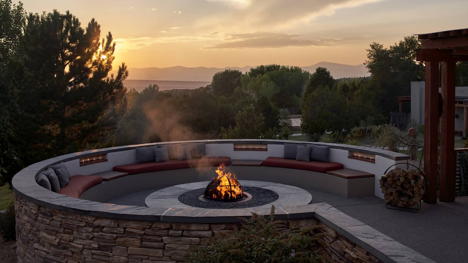 A firepit outside during a sunrise, surrounded by trees and plants.