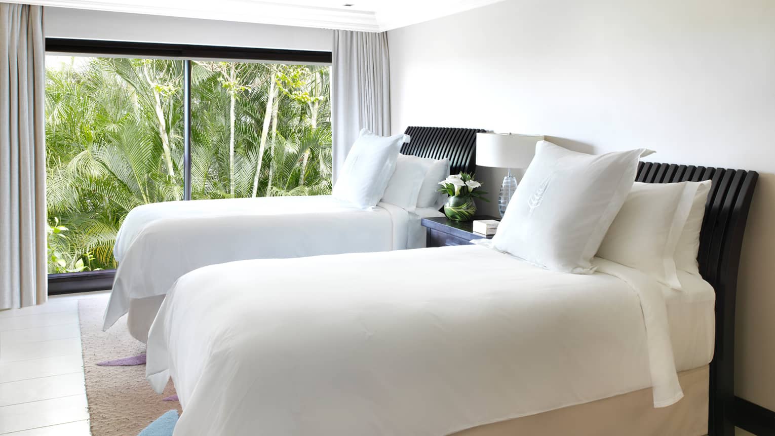 Two single beds with white linens, pillows in bright room by floor-to-ceiling window