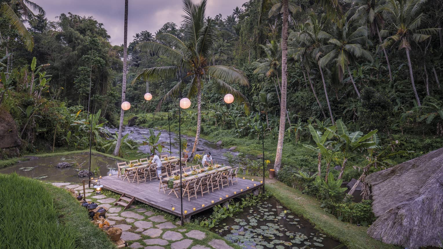 Megibung Dinner is set on a wooden deck as the sun sets beyond lush trees