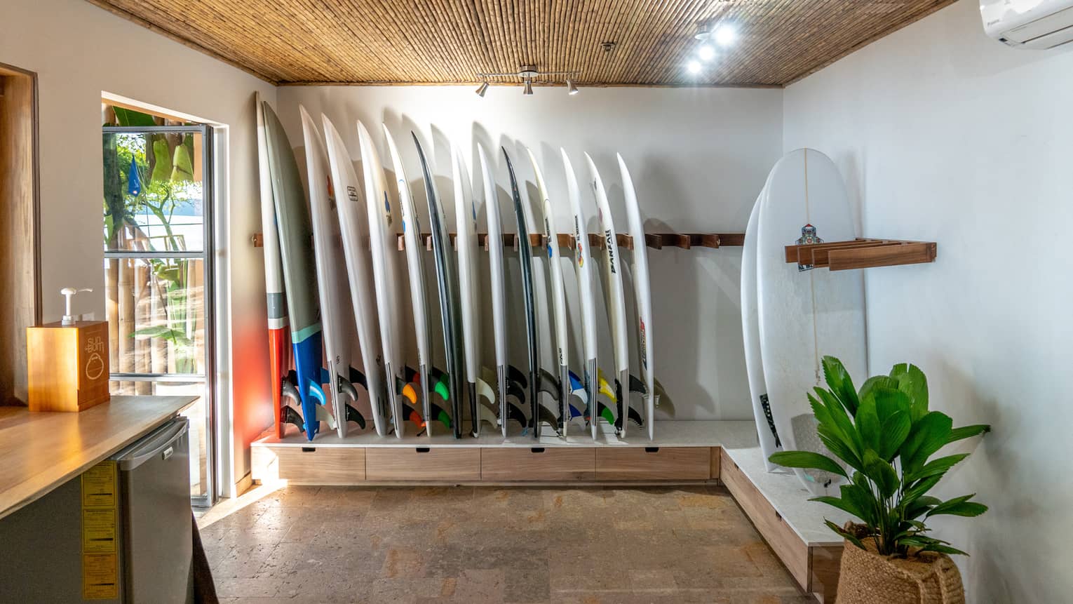 Interior of a small surf shop with crisp white walls, bamboo ceiling and a row of surfboards lined up along the wall