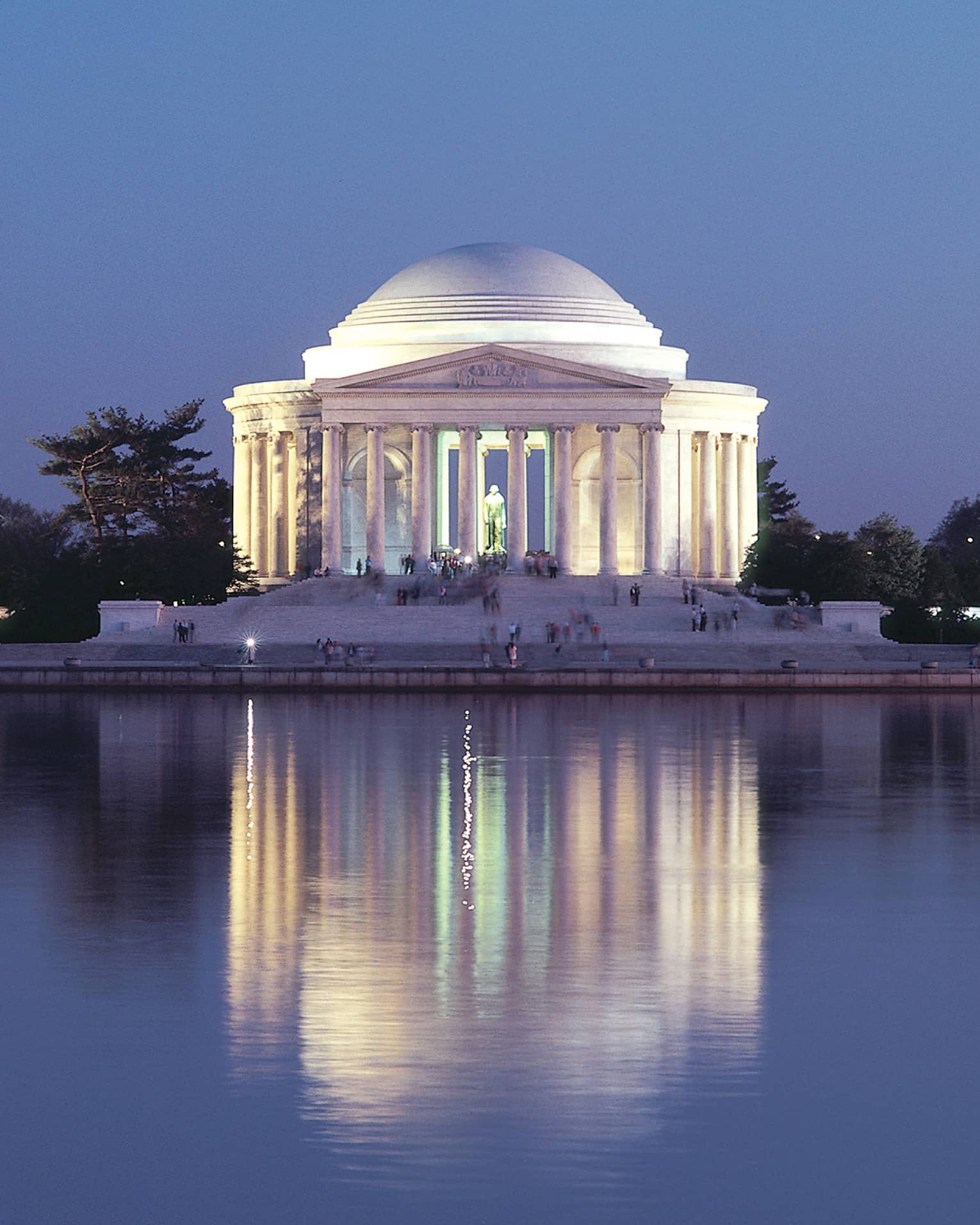 A large historical monument of white pillars and a large dome next to water.