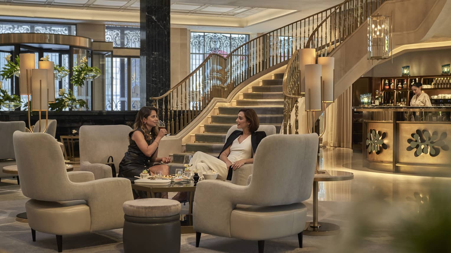 Two guests sitting in a hotel lobby vignette beside a grand staircase