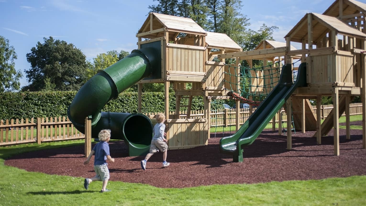 Two young children running towards a playgrounds on a sunny day outside.