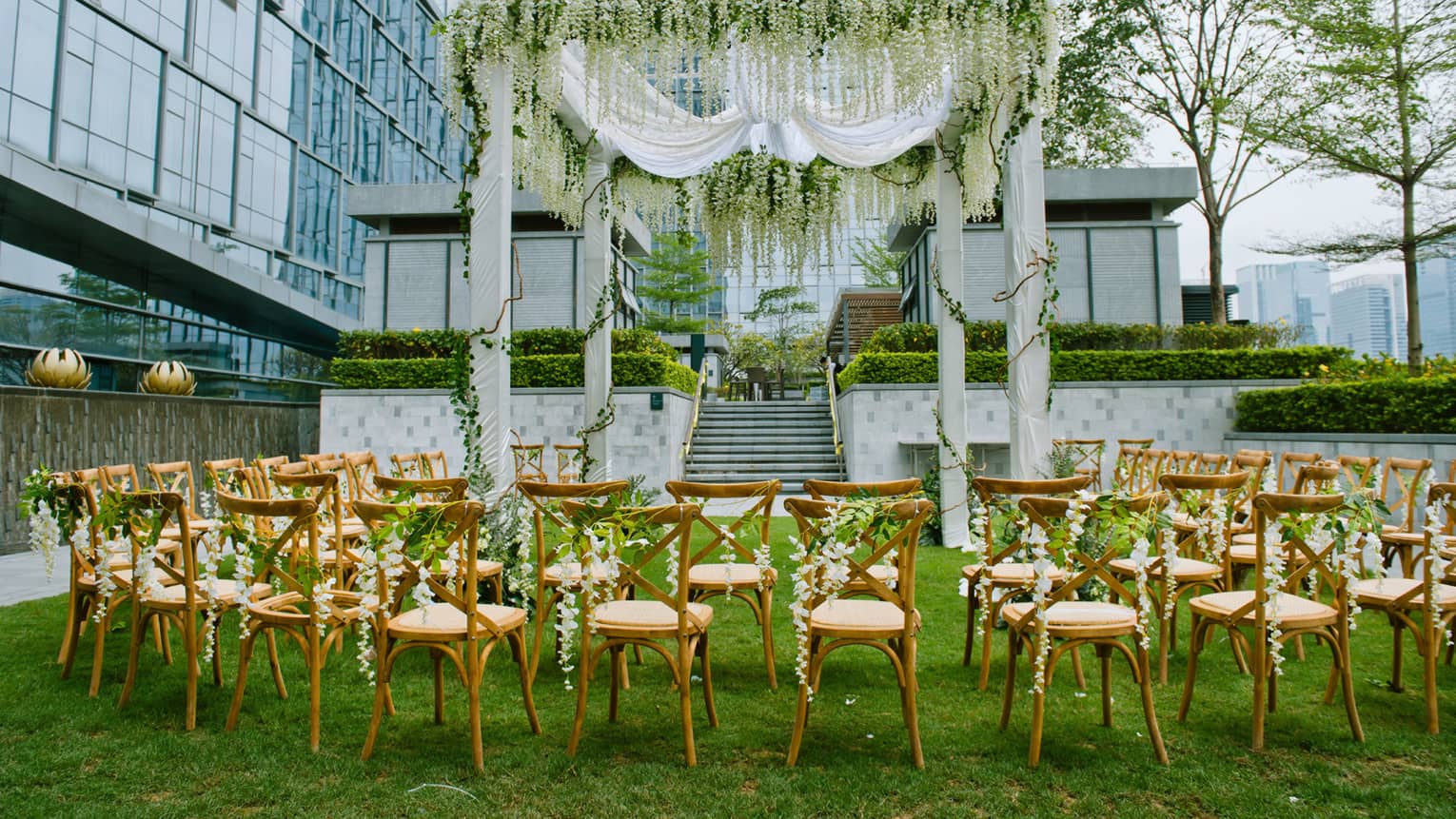 Wedding on event lawn, rows of chairs under large altar with white fabric, vines 