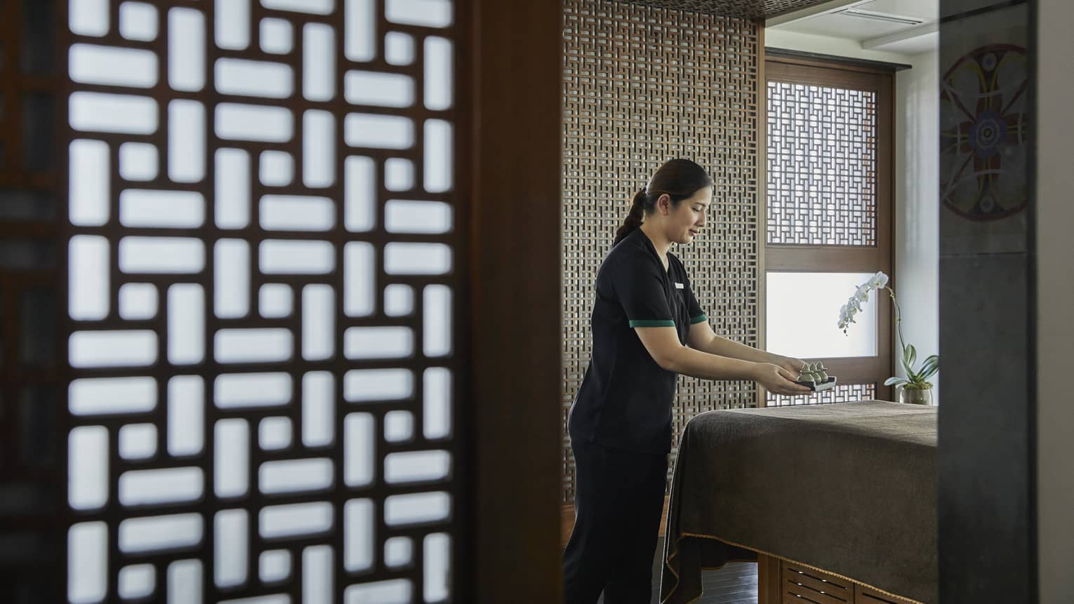 A female esthetician prepares a bed in the massage room. 