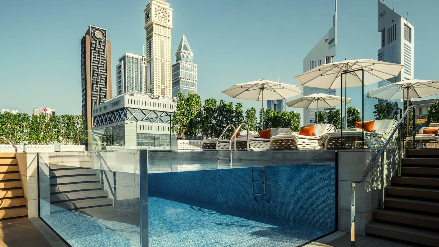 Raised glass plunge pool by stairs on patio deck, lounge chairs, umbrella