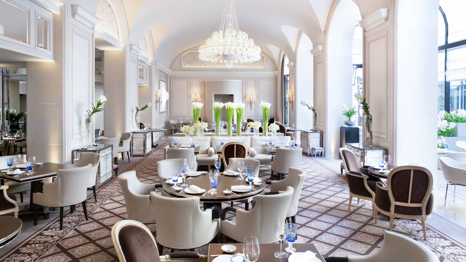 Bright Le George dining room, white chairs around tables under arched pillows, chandeliers