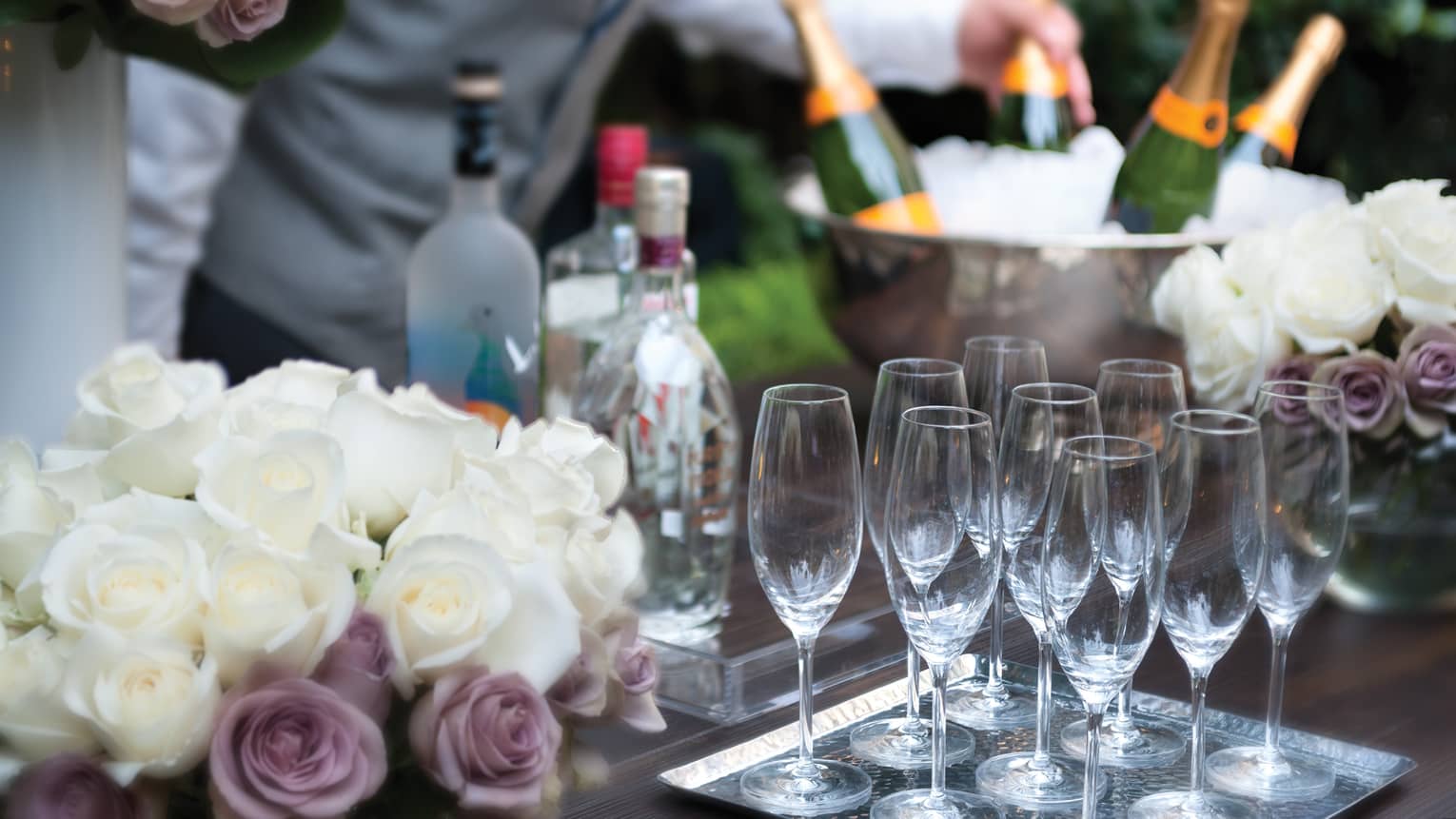 Close-up of white and purple roses, empty Champagne glasses on tray in front of ice bucket, bottles