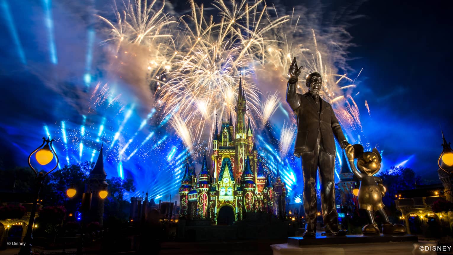 Fireworks and blue lights fill the night sky above the monument of Walt Disney at Disney world in orlando florida