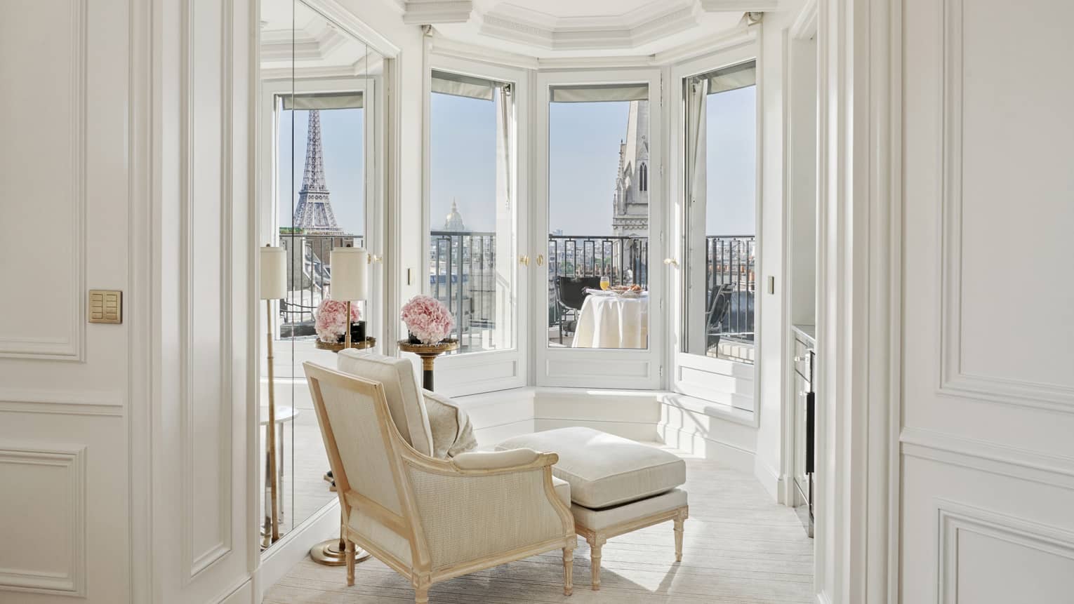 A white room has windows and a balcony with a direct view of the Eiffel Tower