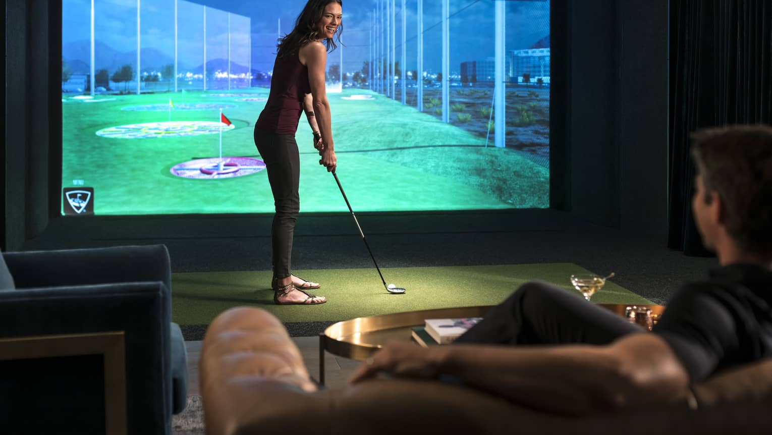 A woman prepares to swing a golf club in front of a virtual golf simulator screen