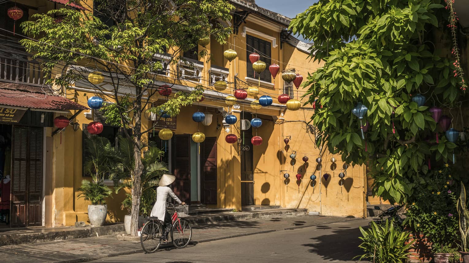 A woman biking down a historic street in Hoi, Viet Nam with lanterns along the side of a house 