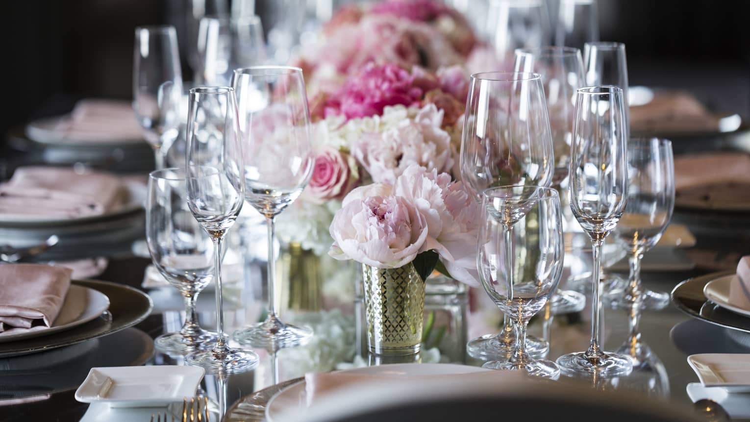 Pink roses, empty wine glasses arranged on long wedding banquet table